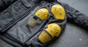 Close-up illustration of a commuter motorcycle jacket showing removable CE-rated armor pads at the shoulders and elbows.