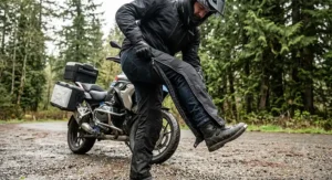Rider stepping into men's riding overpants with full-length side zippers over street pants for quick rain protection.