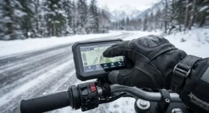 A close-up view of touchscreen-compatible fingertips on waterproof winter motorcycle gloves tapping a handlebar GPS unit.