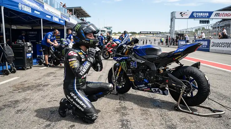 A rider wearing racing boots for short riders while adjusting gear in a sunny paddock.
