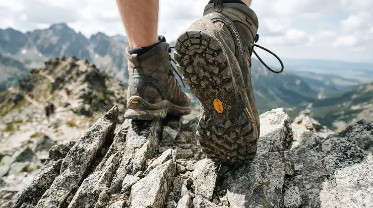 Close-up of off-road motorcycle boots for trail riding featuring durable rock guard soles on uneven terrain.