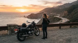 A rider leaning against a motorcycle at a scenic coastal overlook wearing women's motorcycle sneakers for casual riding.